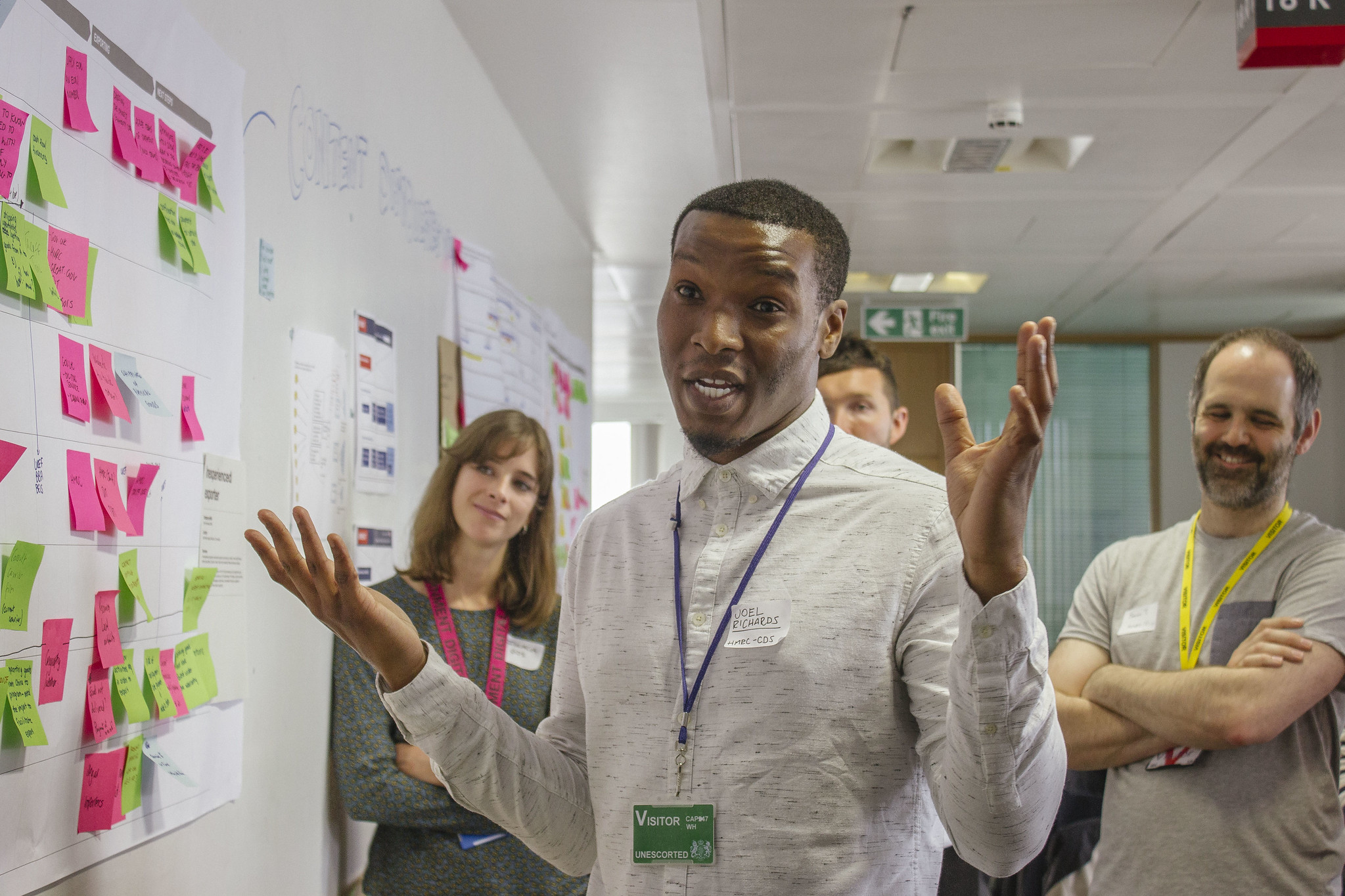 Image of a man participating in a workshop. Behind him there are other people. And on his left there is a wall with coloured post it notes